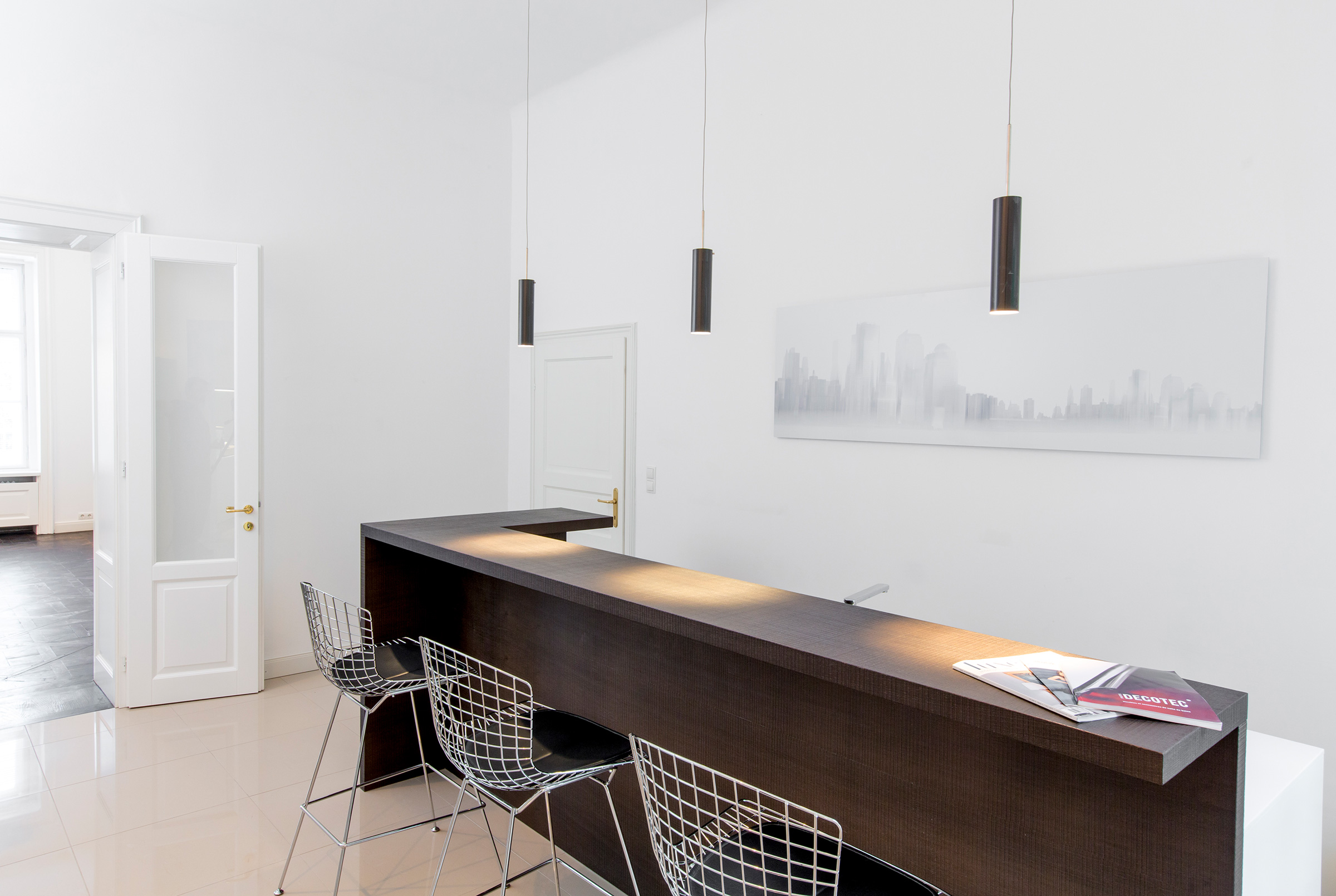 View through panelled doors into a salon with blue artwork and pendant lights