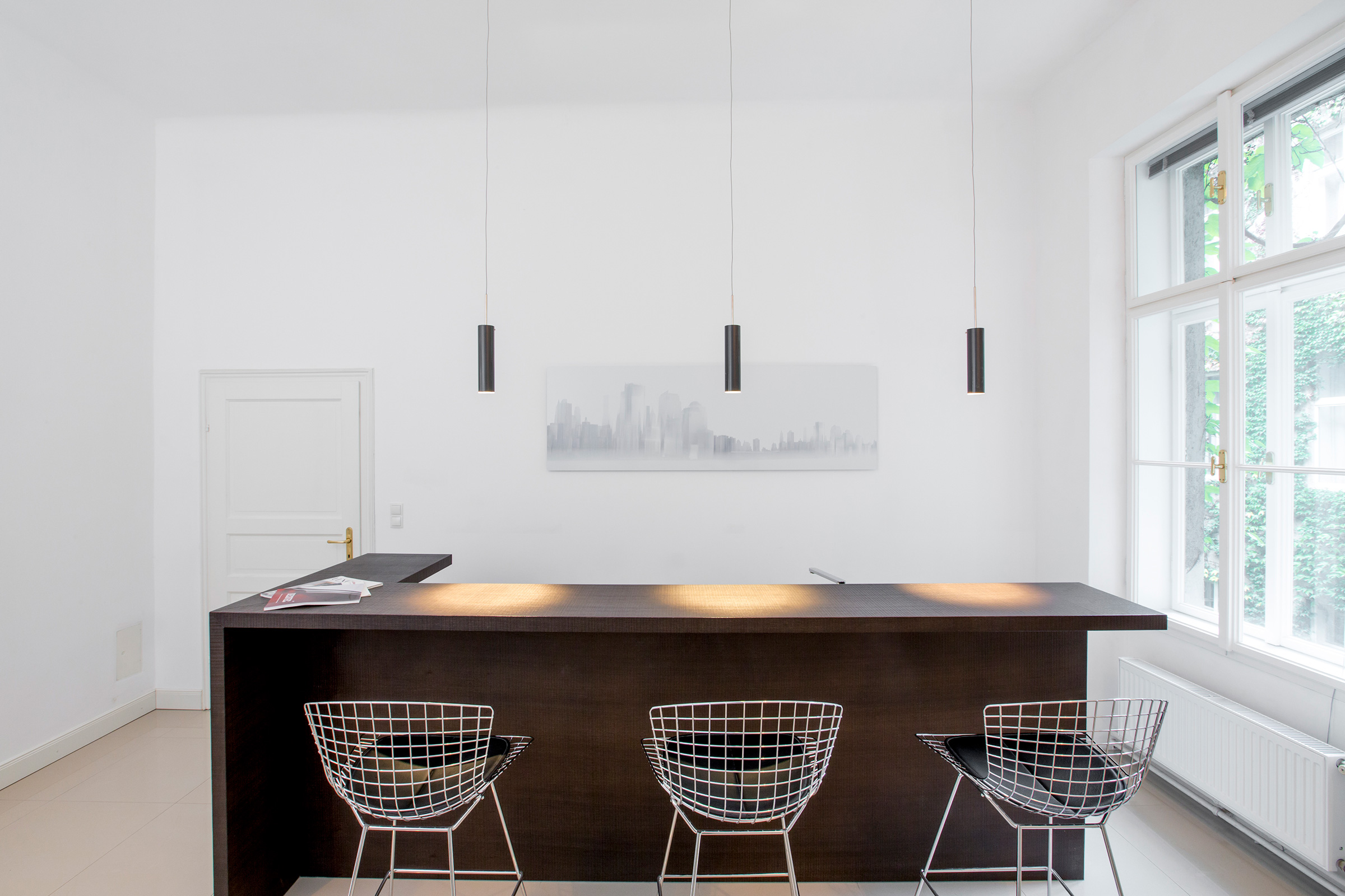 Bright minimalist kitchen bar with dark wood counter, wire bar stools and pendant lights